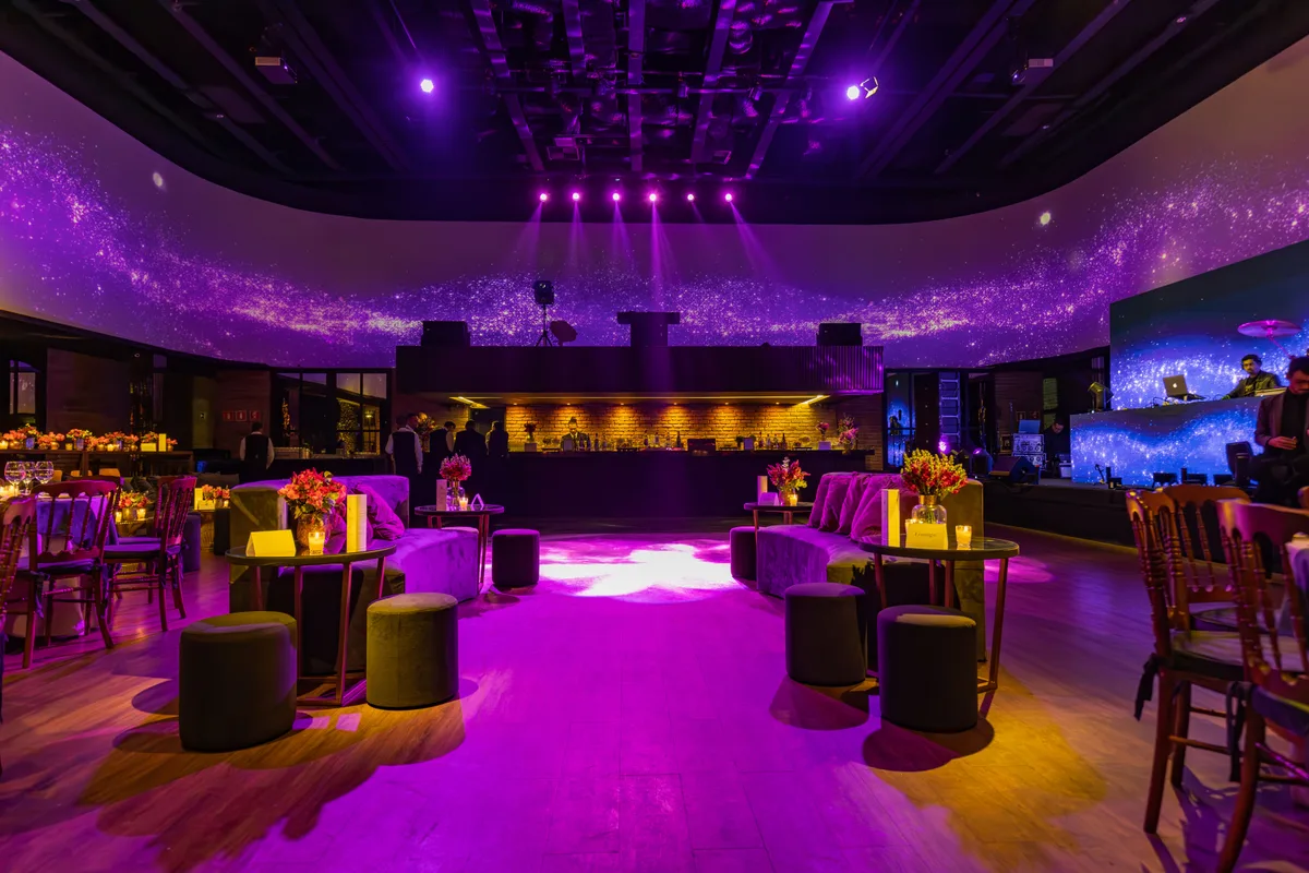 Een evenementenruimte met loungeplekken, dansvloer en paarse showverlichting