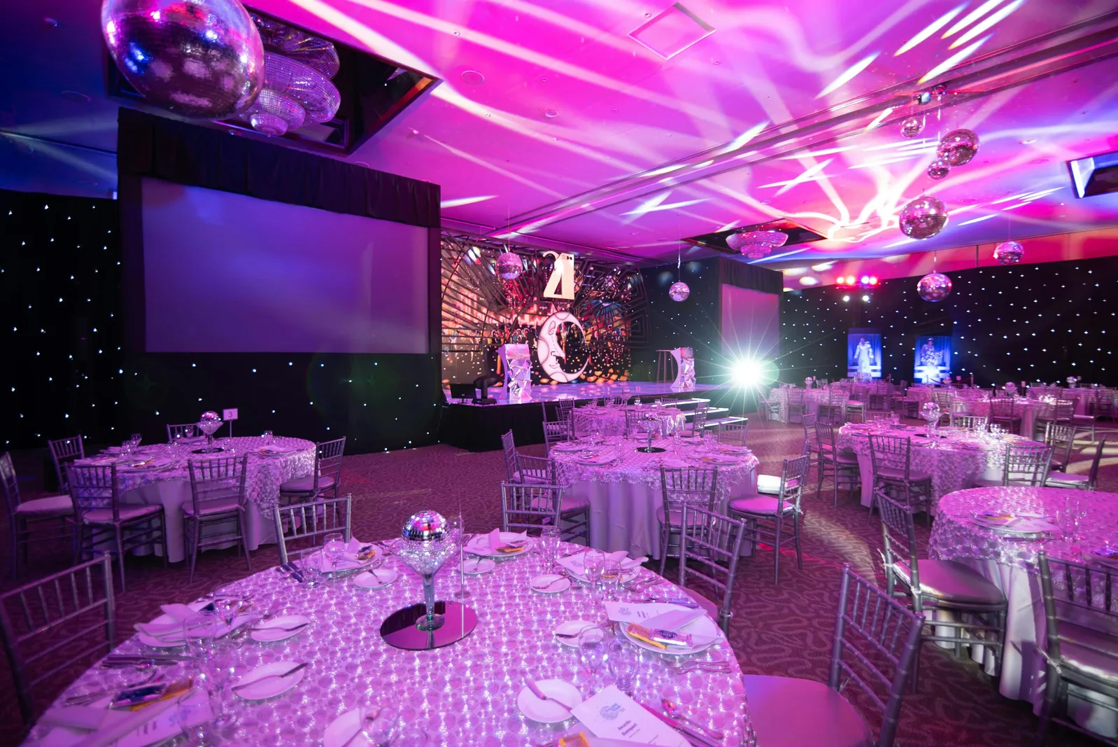 Zaal vol gedekte tafels met discoballen en showverlichting tijdens een dinnershow