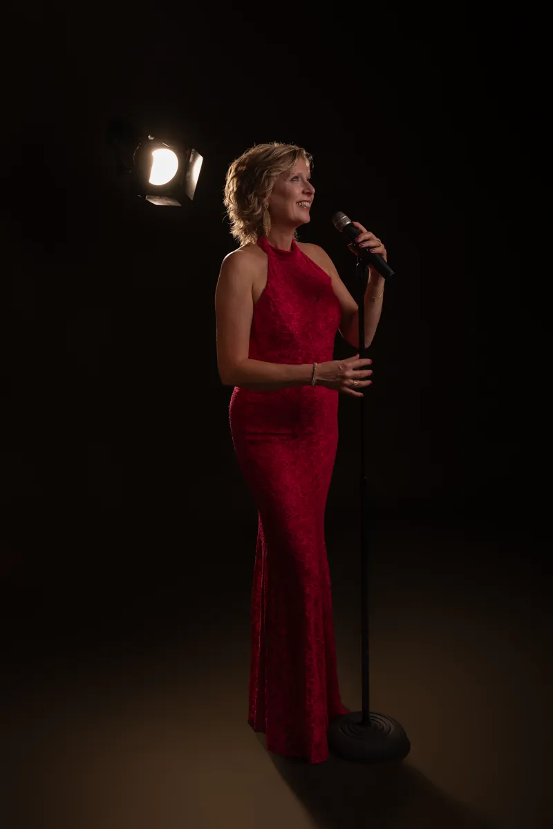Josefine Wijnhoven in een rode jurk, zingend onder een spot