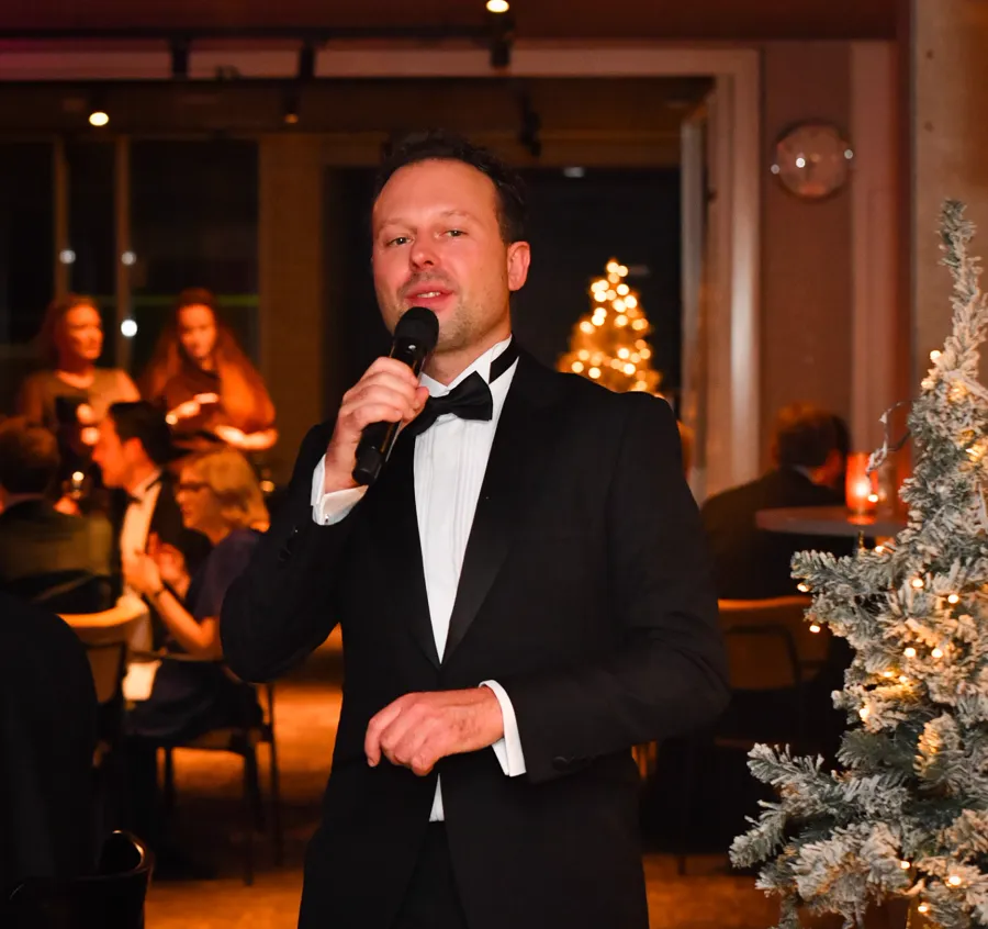 Raoul Wijsma in smoking, zingend tussen de gasten bij een kerstdiner